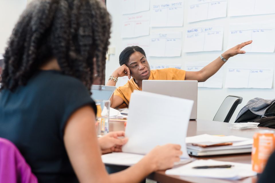 Two women at a conference table, one is speaking