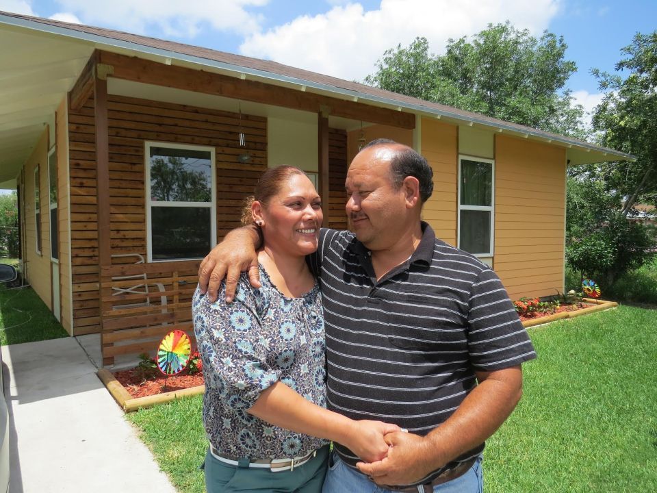 Smiling couple standing with their arms wrapped around each other in the front yard of their home. 