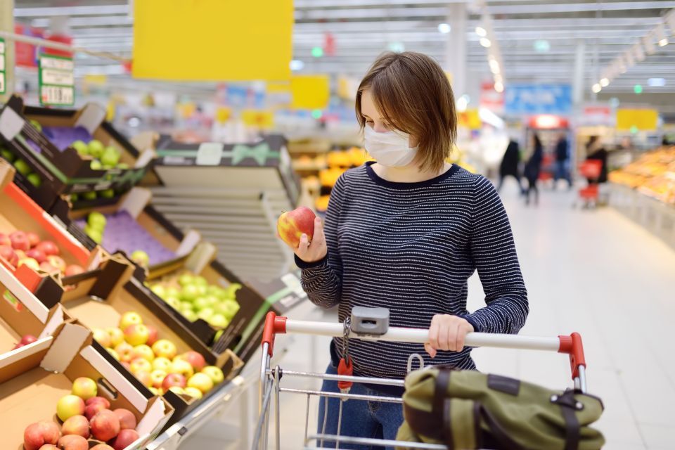 Woman with mask shopping in fruit section of grocery store