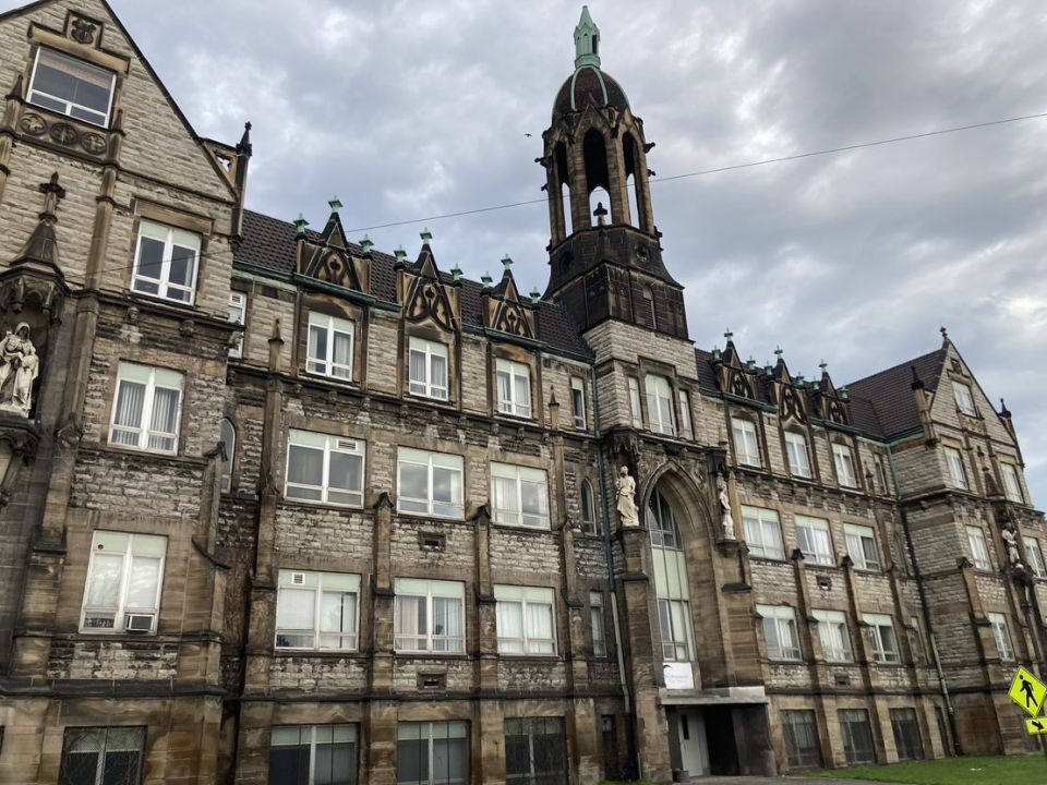 A historic school building with a bell tower against a cloudy sky backdrop.