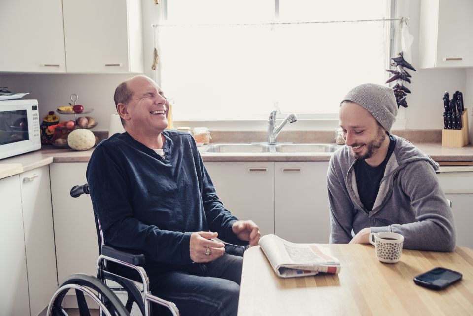 Man in wheelchair laughing with a man seated at a table