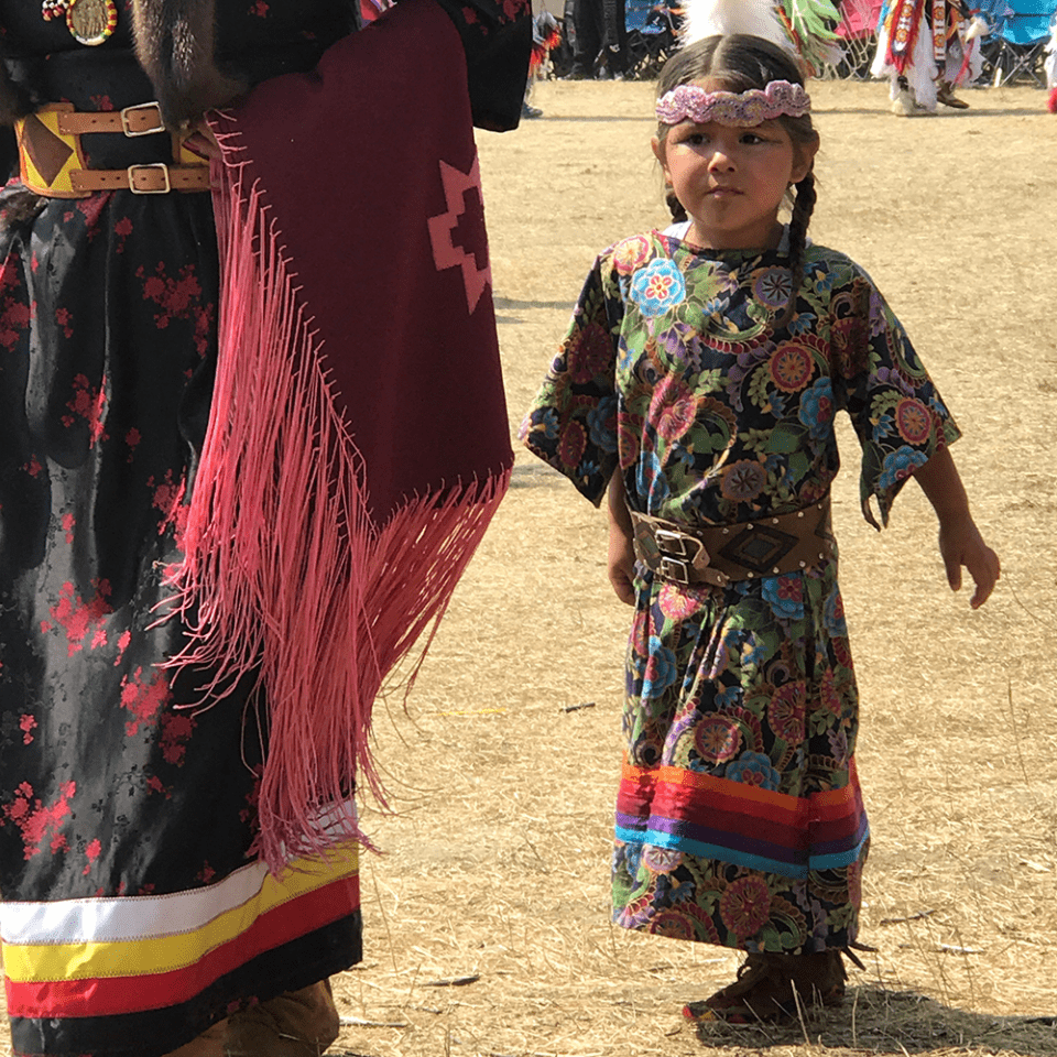 A little girl in Native regalia standing outside