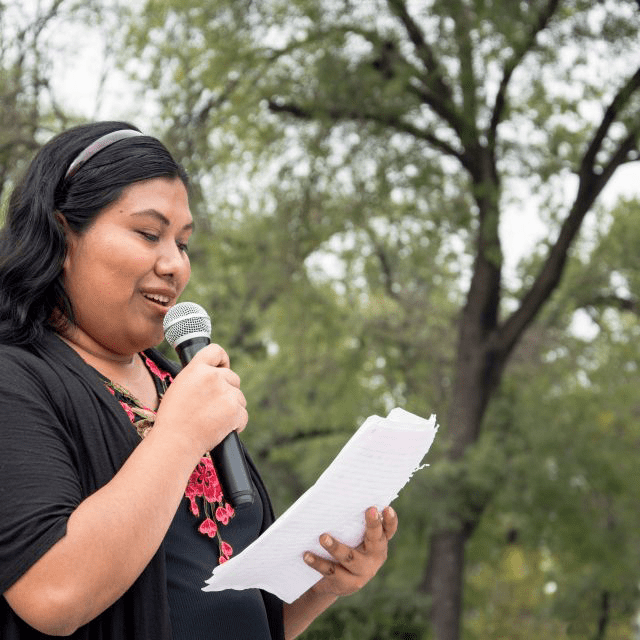 A person holding a piece of paper and reading into a microphone