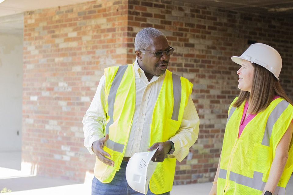 Two construction workers wearing yellow vests talking to each other