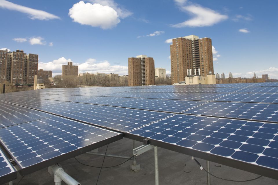 Rooftop solar panels with a blue sky and high-rise buildings in the background.
