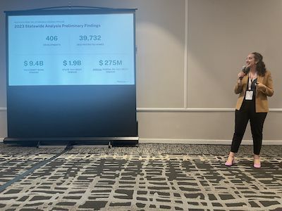 Woman in Brown Blazer and Black Slacks with Microphone Presenting Data