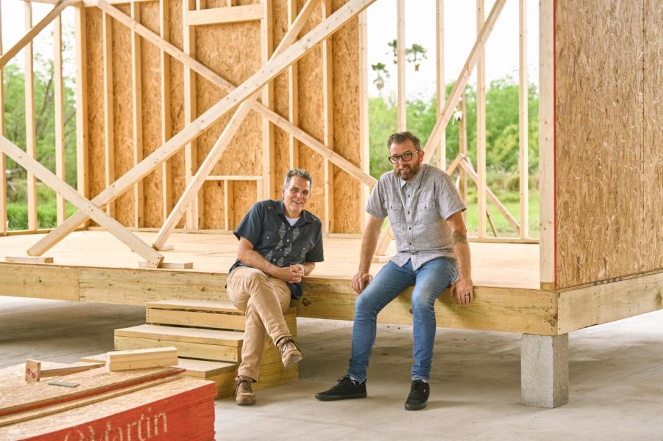 Two men sit on the floor of a modular home under construction.