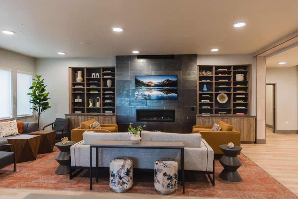 Attractive community room with a terra cotta-colored rug, beige couch, and a fireplace wall made of natural stone.