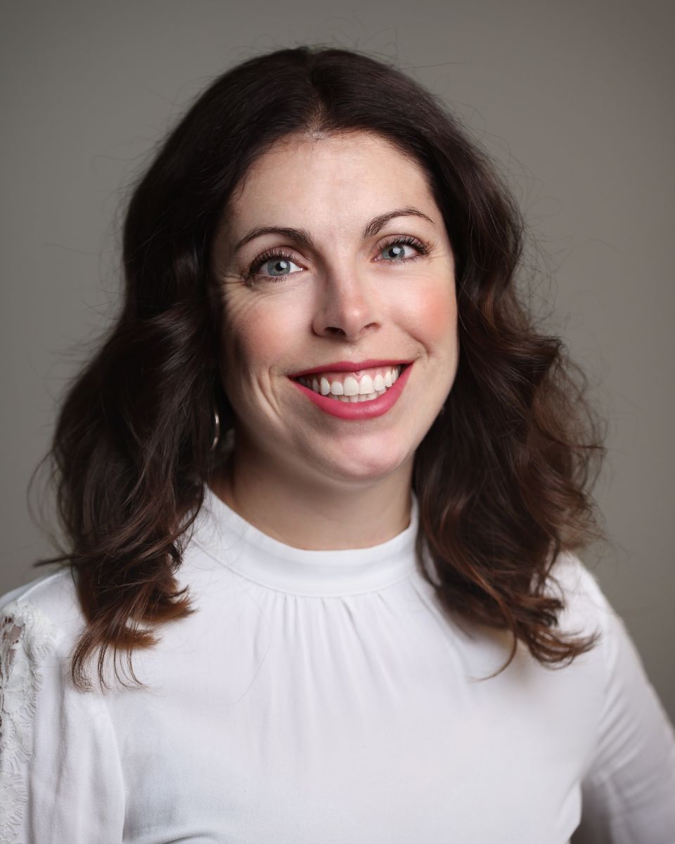 Person smiling with shoulder-length brown hair wearing a white top.