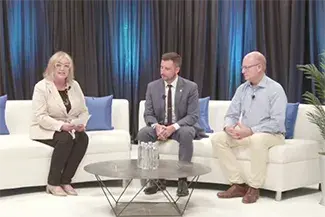 Three people sitting on white couches with a coffee table in front of them