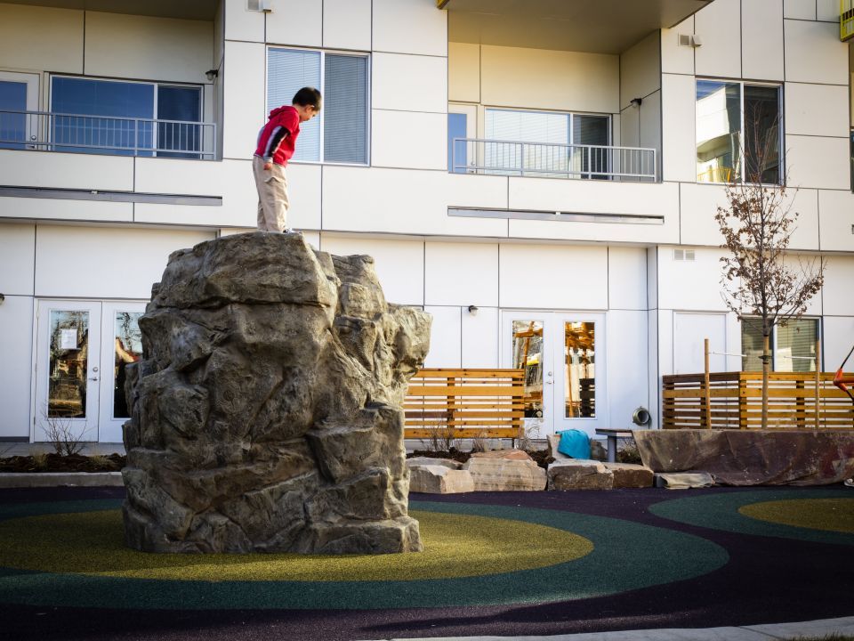 Child stands on a rock in the middle of a play area in a courtyard