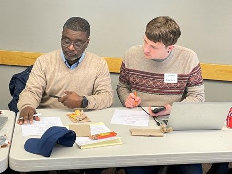 Two people sit at a desk reviewing documents and working together