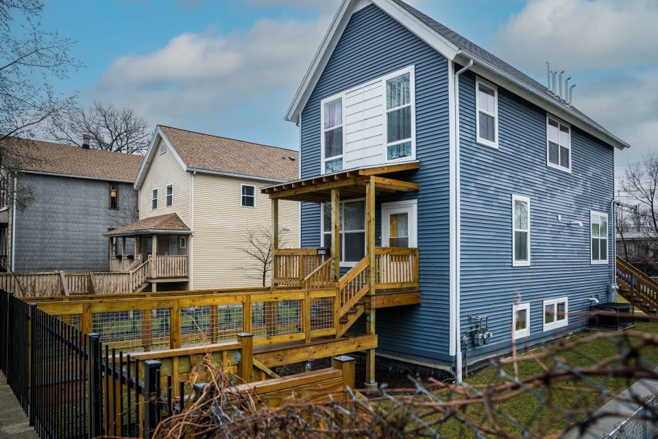 Light blue house with a wooden porch and fencing with an A-frame roof.