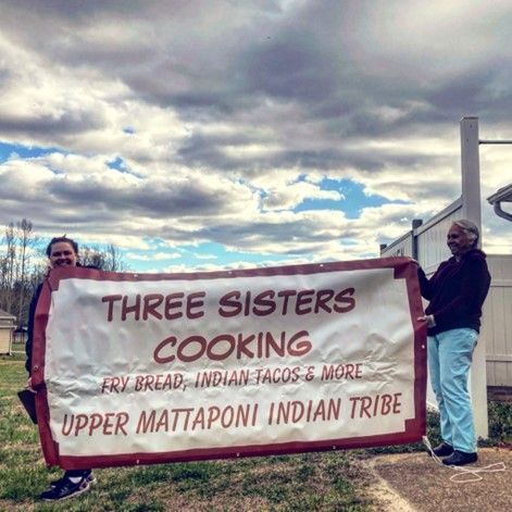 Two people holding a banner that says: Three Sisters Cooking Upper Mattaponi Indian Tribe