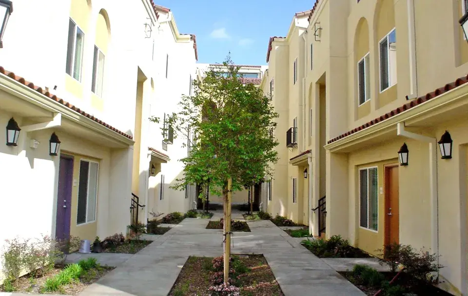 Multifamily housing development with two rows of tan-colored 2-story homes facing each other with trees in the middle