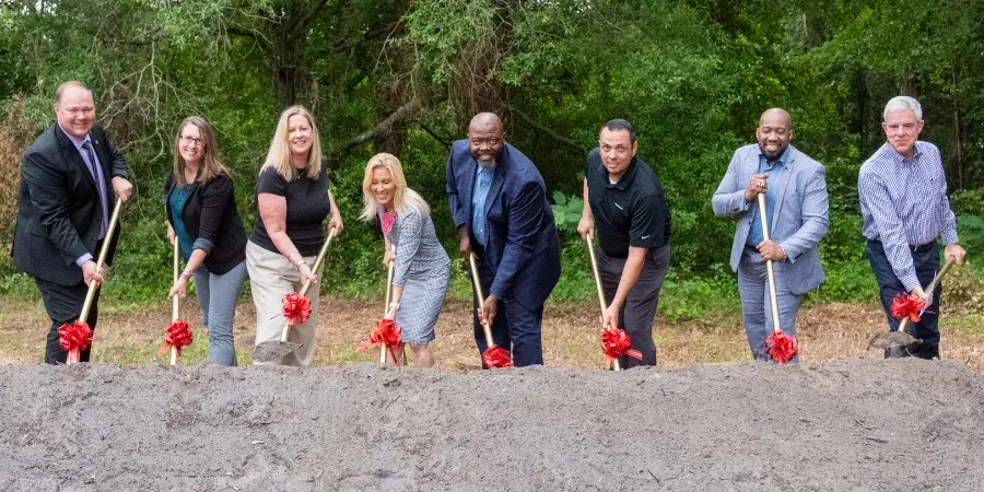 Group of professionals posing for a groundbreaking with shovels and dirt
