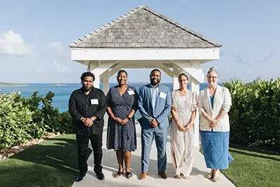 A group of five people stand in front of a gazebo that overlooks the ocean