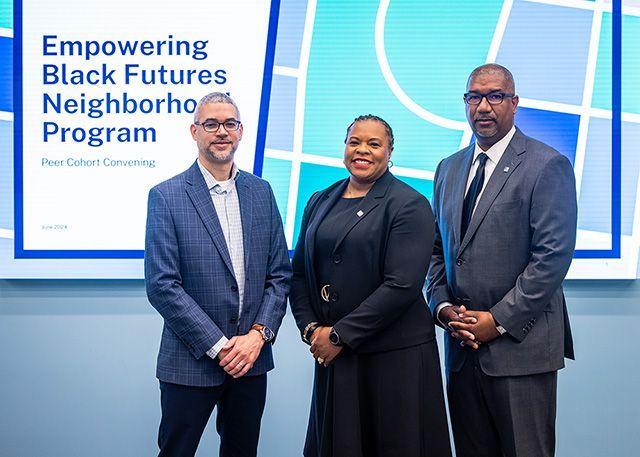 The people in blue, black and gray suites standing in front of a screen