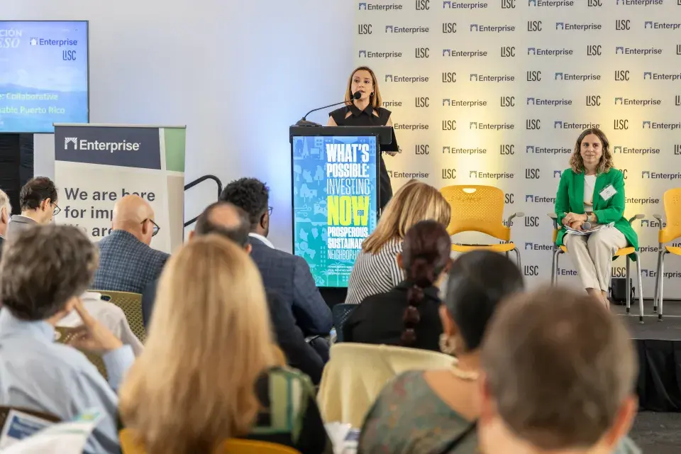 Person at podium speaks with another person seated on stage in front of audience