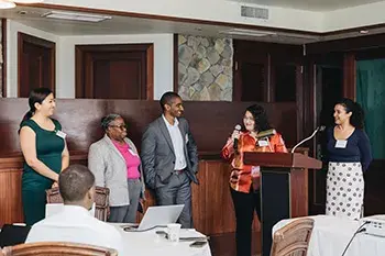 Five people stand by a podium as another person seated looks on. Credit: Nicole Canegata