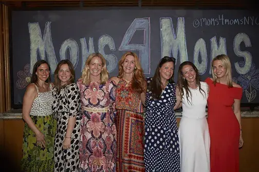 Members of Moms4Moms stand in front of a wall with Moms4Moms drawn in chalk
