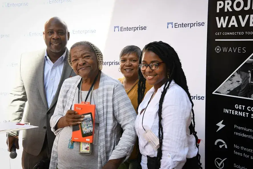 A group of people stand in front of a wall with the word Enterprise and a Project WAVES sign