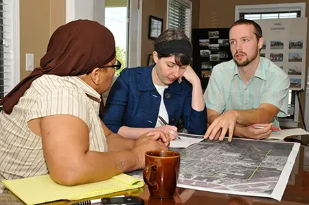 A man talks with two women at a table with a poster on it