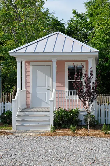 A small blush colored cottage with a white roof and steps with trees in the backyard