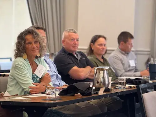 Five people behind a table looking forward and listening to off-camera speakers