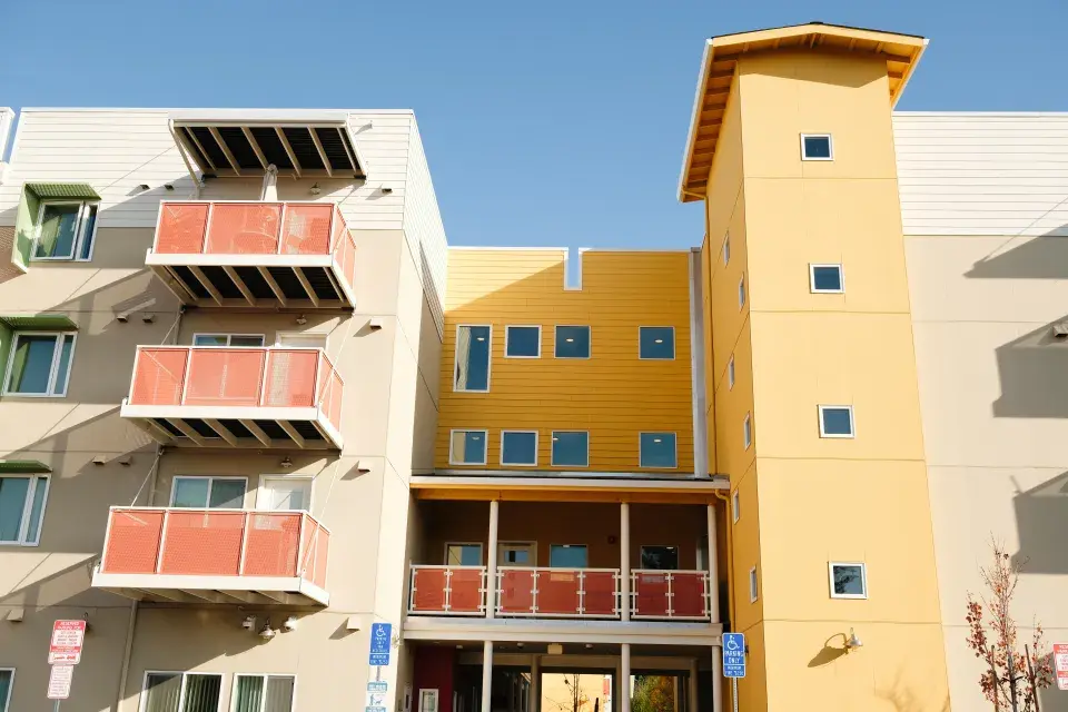 An apartment building with yellow painted columns and brick colored balconies