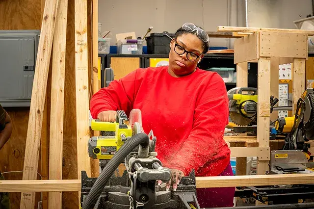 A student in a red shirt using a table saw