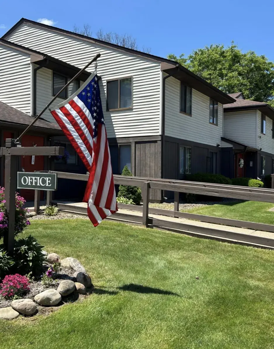 Dark brown and beige two story apartment building with USA flag and office sign in the foreground