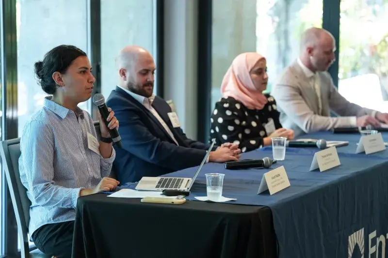Woman speaking into microphone seated with three other people at a table