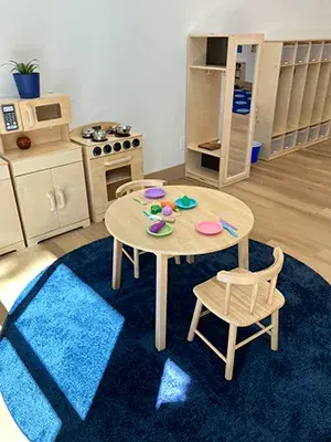 A children's kitchen area with a round table and two chairs, cubbies line the wall in the back 
