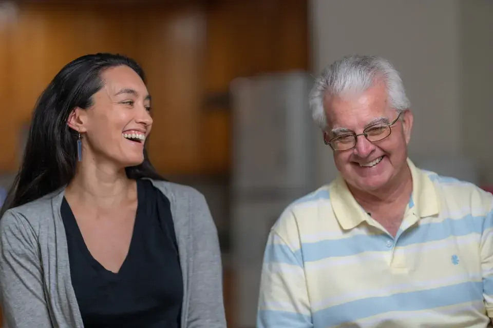 Two people sit side by side smiling and laughing.