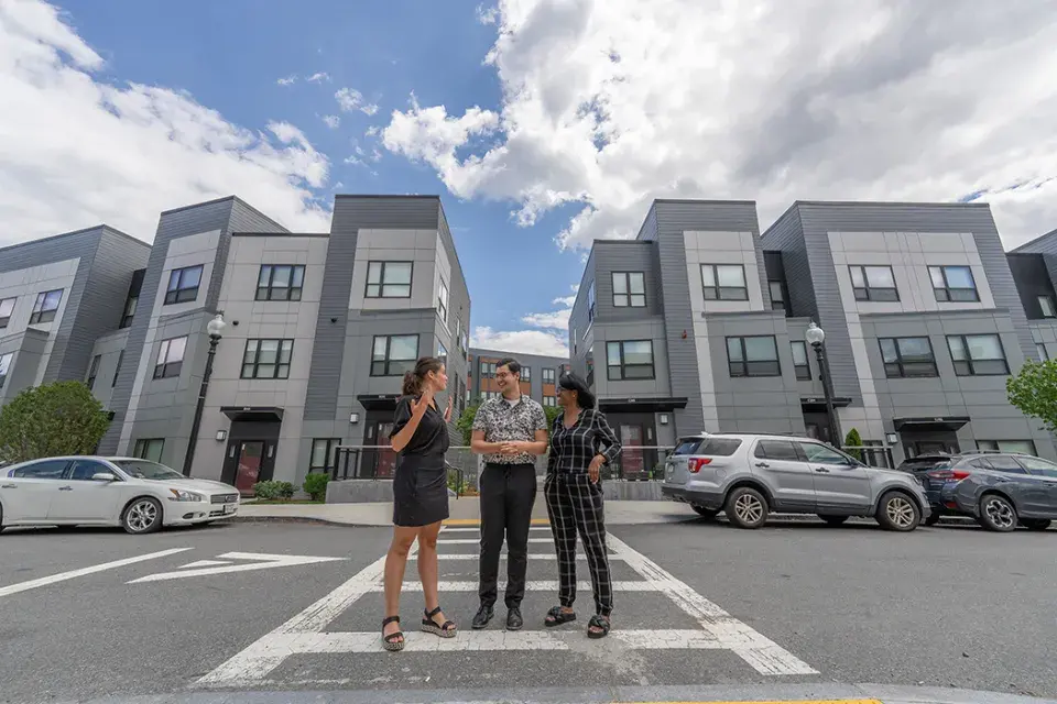 Three people standing in a parking lot in front of homes talking.