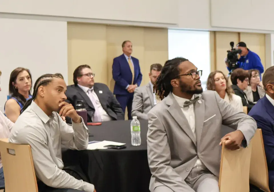 Group of people sit at round table looking and listening attentively 