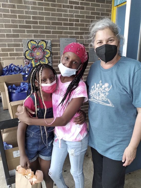 Two girls and an adult woman in front of boxes filled with packed reusable bags