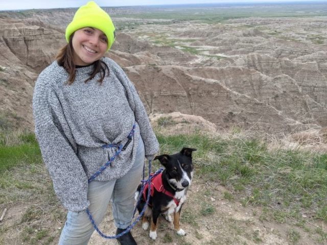 Caitlin Buro in a neon yellow hat, sweater and jeans with a dog outdoors