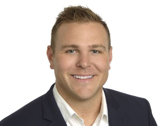 Man with short amber-colored hair wearing a white collar dress shirt and black suit jacket.