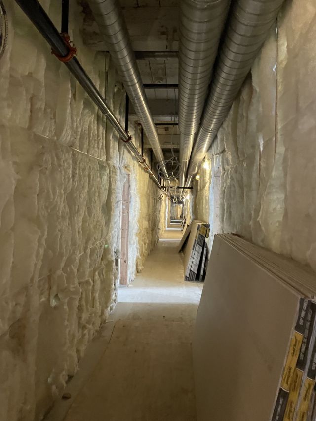 Construction project showing insulation and ceiling pipes lining a long hallway.