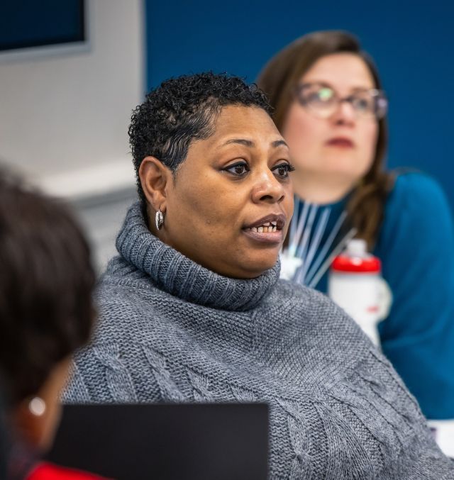 Person with short black hair and silver hoop earrings wearing a grey cowl neck sweater