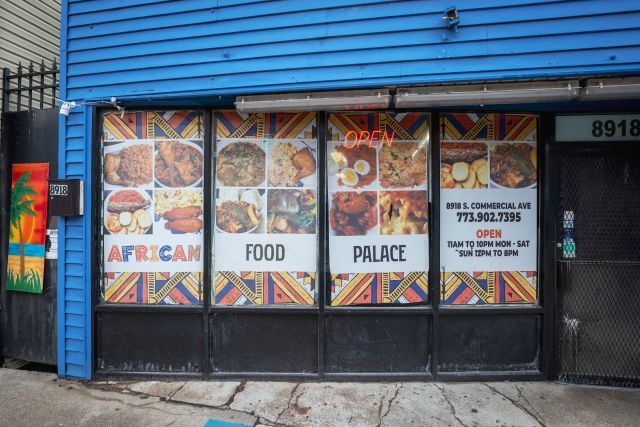 A storefront with a bright blue awning and its name African Food Palace on the window along with photos of different types of food.