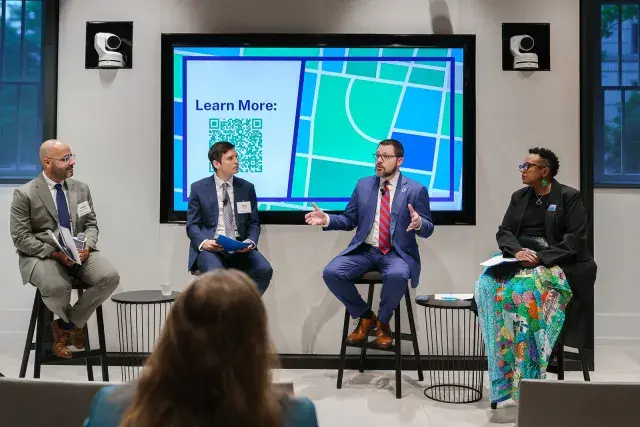 Four people sit on stools conversing with an audience in front of them