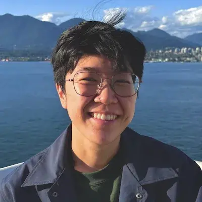 Smiling person with glasses and jacket standing in front of lake