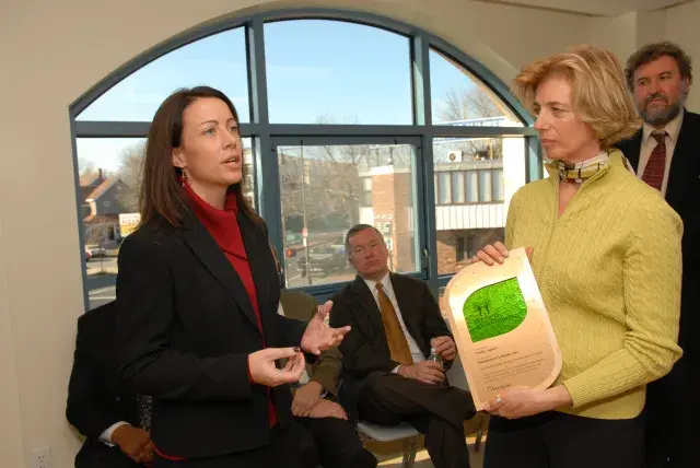 Person speaks while another holds a plaque and listens