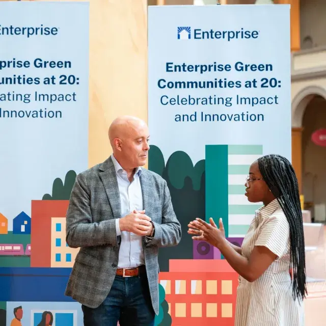 Two people stand talking in front of signage that reads "Enterprise Green Communities at 20"