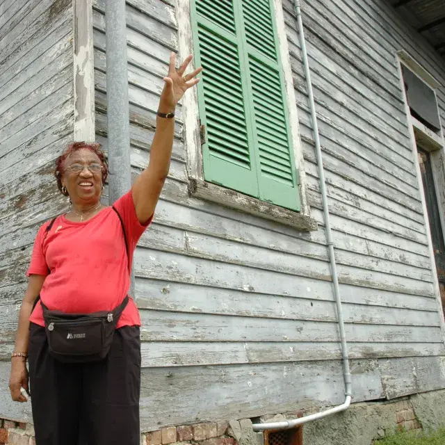 Woman waves in front of a home painted white with green shutters