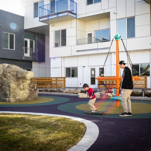 A teenager watches his younger brother on a skateboard at a playground