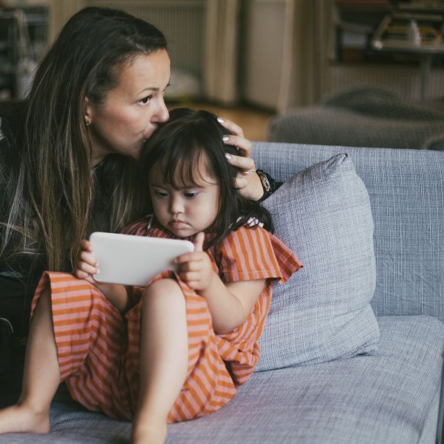 Mother kisses her child's head while sitting on a couch